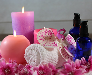 Bild von zwei Kerzen, Blumen, zwei Ölflaschen und einem kleinen Handtuch, die die japanischen Massagen symbolisieren. Dieses Bild gehört zu der Bildergalerie, die Bilder über die verschiedenen in der Praxis der Heilpraktikerin Diane Zardini in Garmisch-Partenkirchen angebotenen Leistungen, enthält.